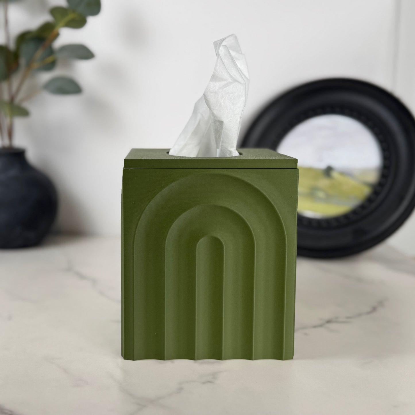 Green tissue box on a marble surface with a plant and vase in the background