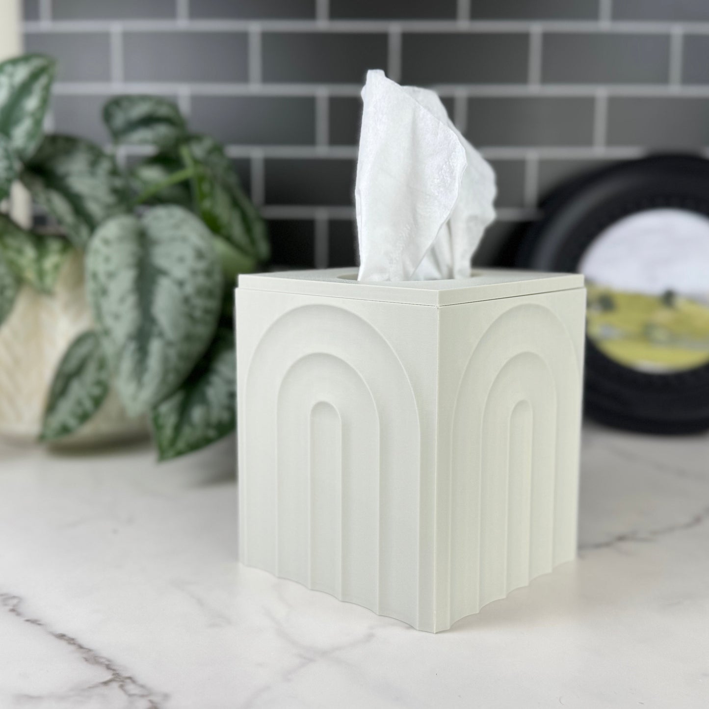 White tissue box with tissues on a marble surface with a plant and records in the background