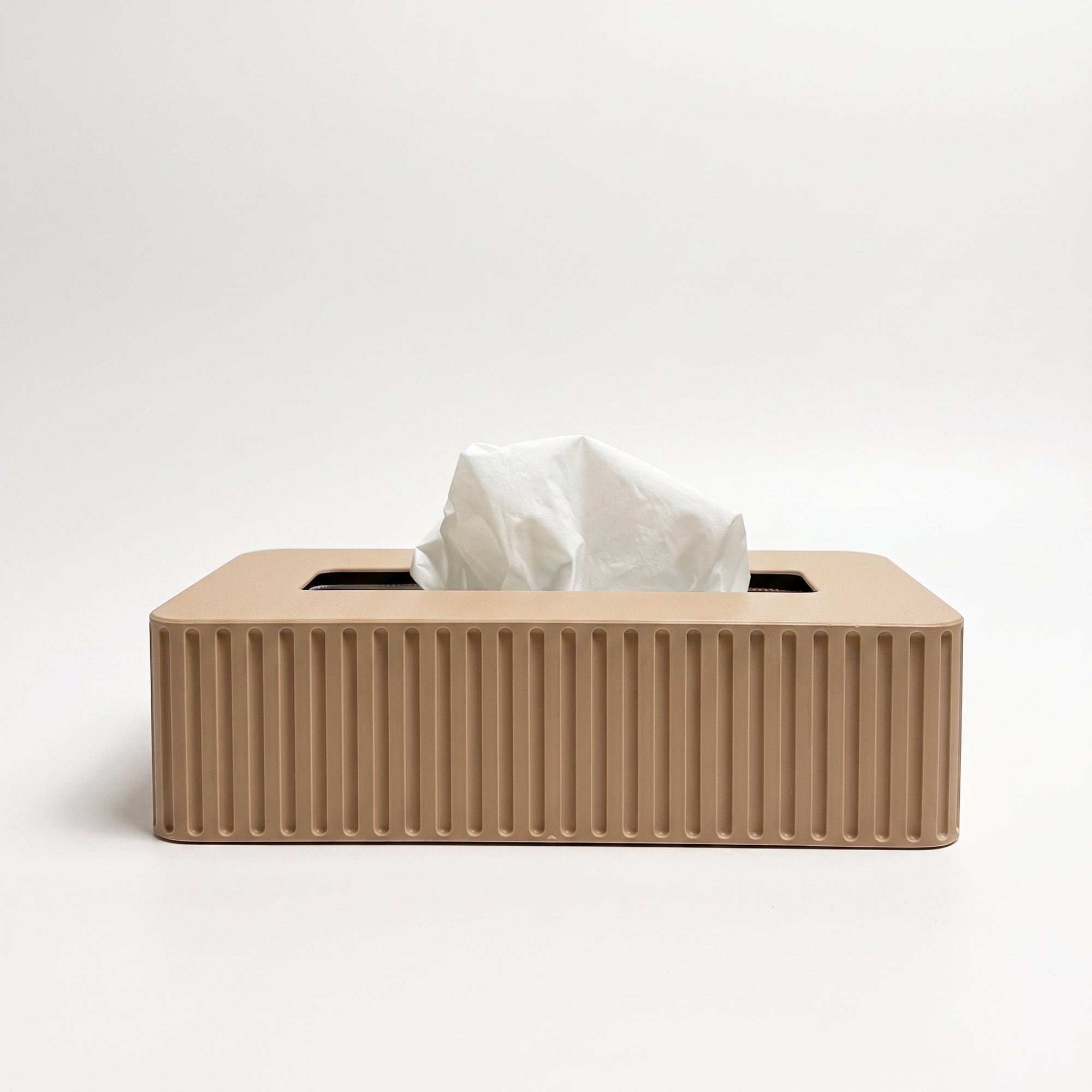 A rectangular tissue box cover in a warm beige color with vertical fluted ridges, shown with a white tissue protruding from the top on a clean white background.