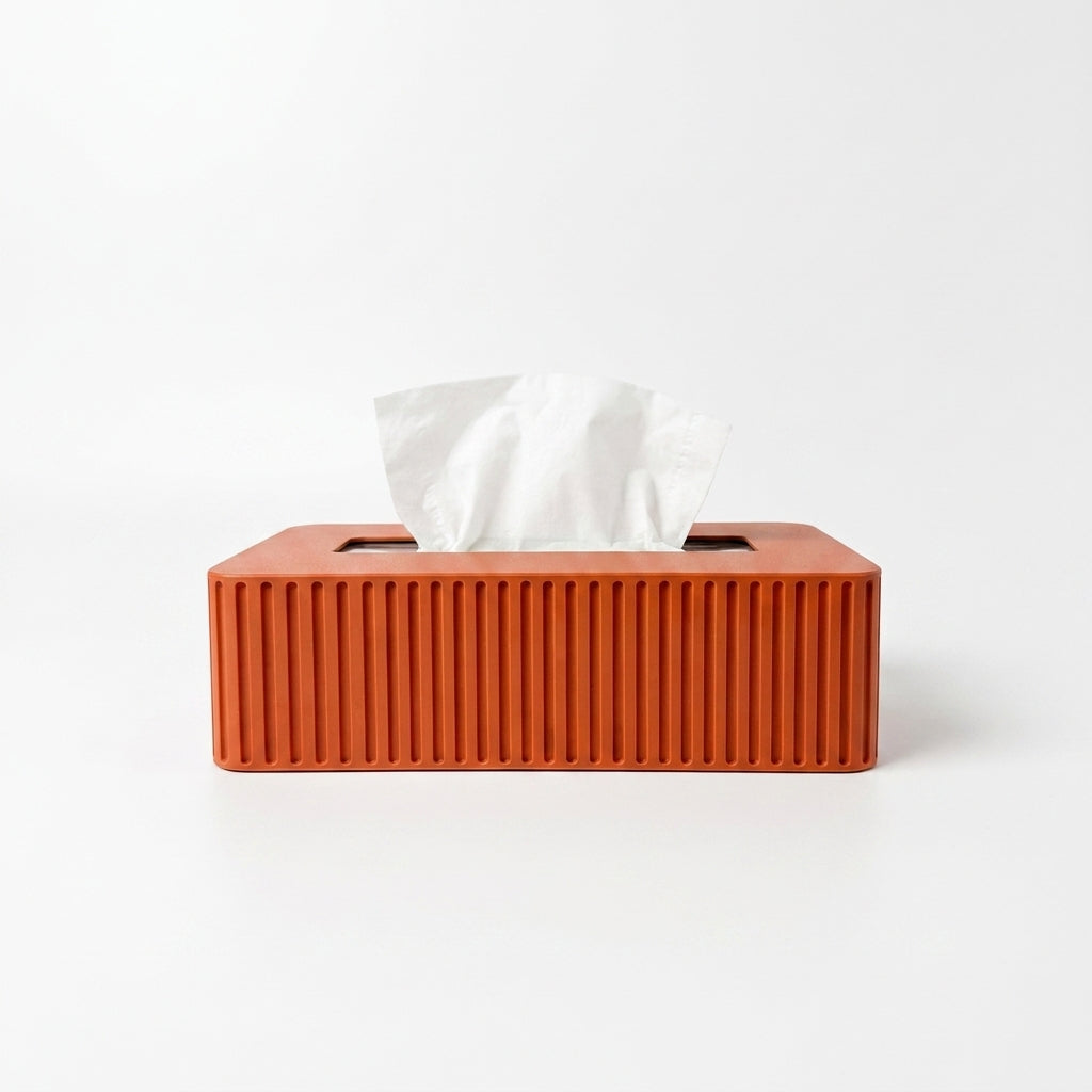 An orange rectangular tissue box cover with vertical ridges and a white tissue paper partially pulled out, set against a plain white background.