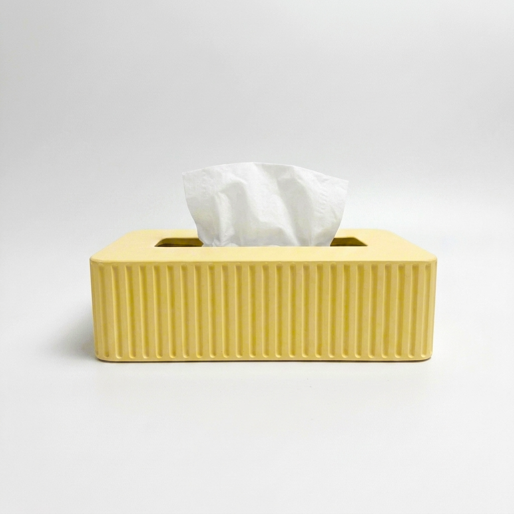 A yellow ribbed tissue box cover holding a white tissue, photographed on a clean light gray studio background.