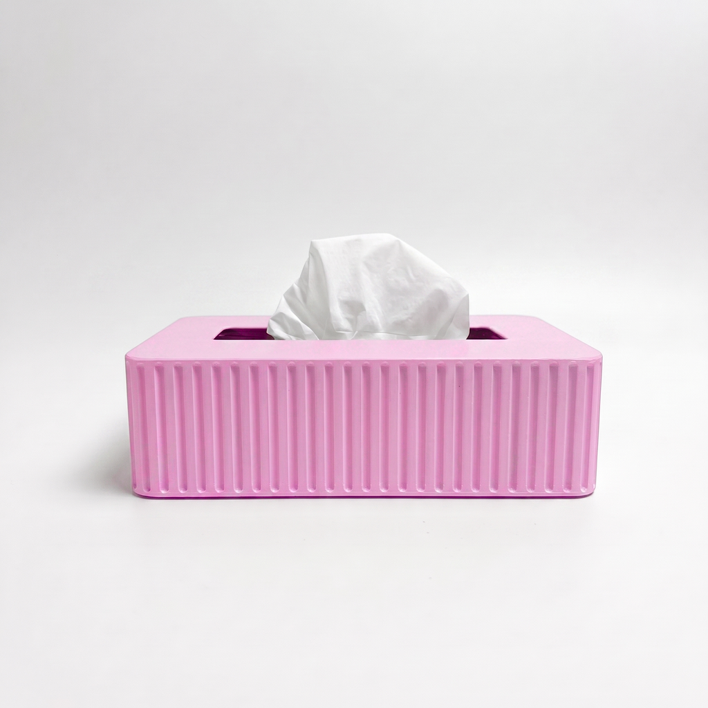 A pink rectangular tissue box cover with vertical fluted ridges on the front, holding a white tissue, photographed on a clean light gray studio background.